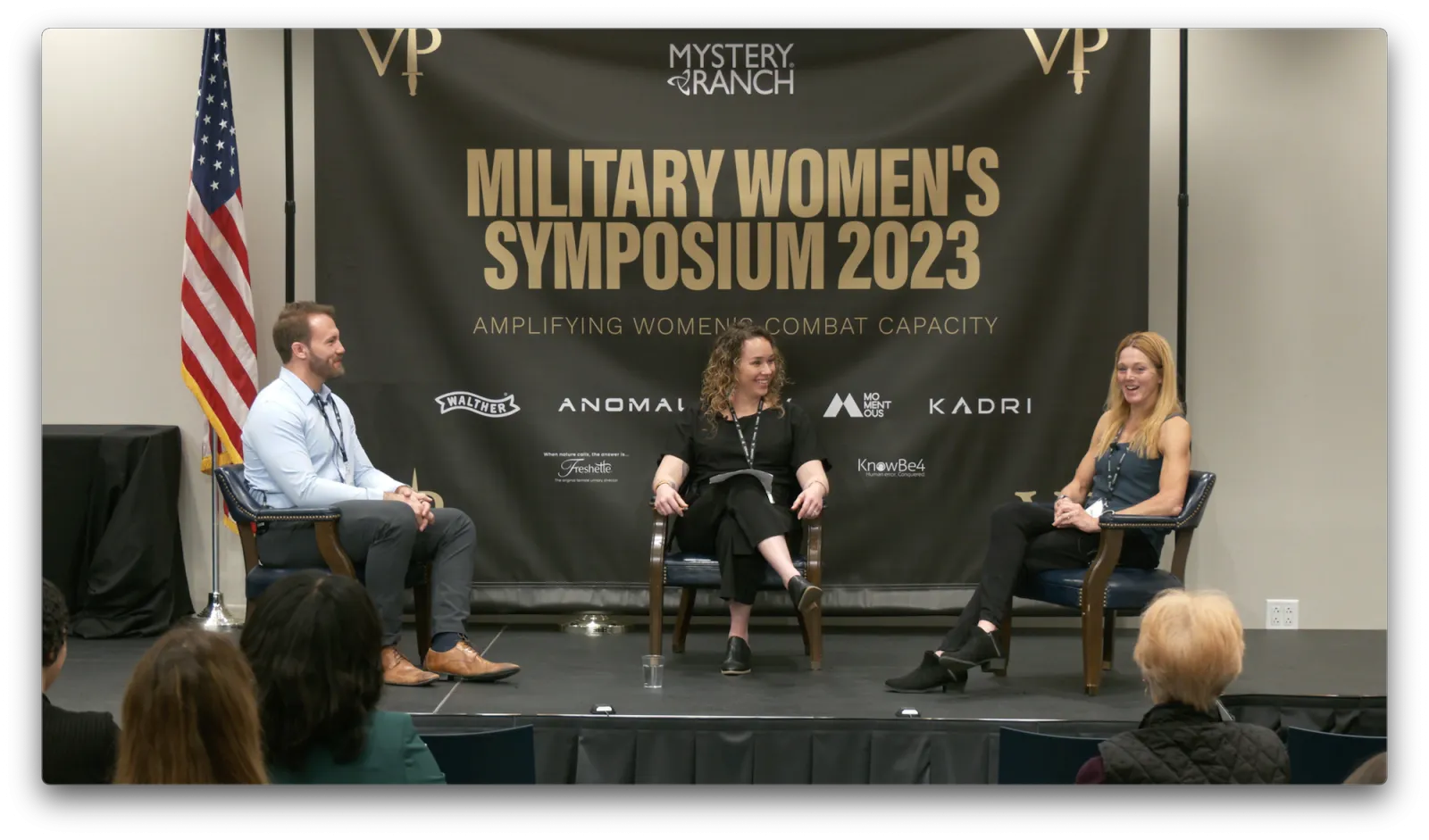 Womens Symposium panel with three people seated on stage.